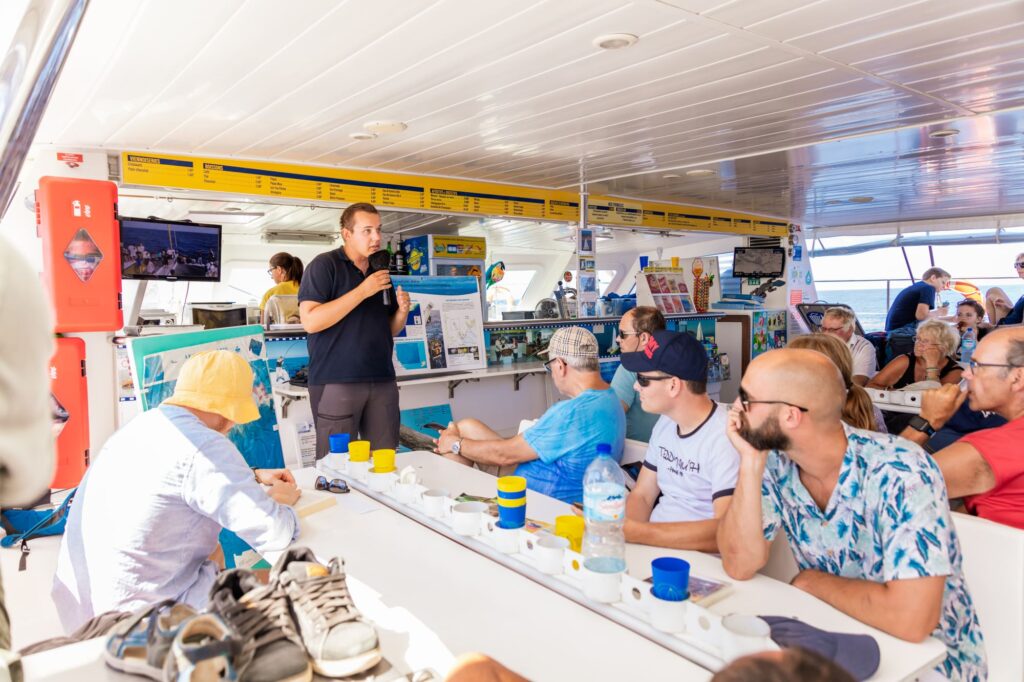 Le guide naturaliste animant une conférence pédagogique sur la biologie et le comportement des Grands Dauphins (Tursiops truncatus) auprès des passagers attentifs lors d'une Excursion dauphins à Canet avec le catamaran Navivoile