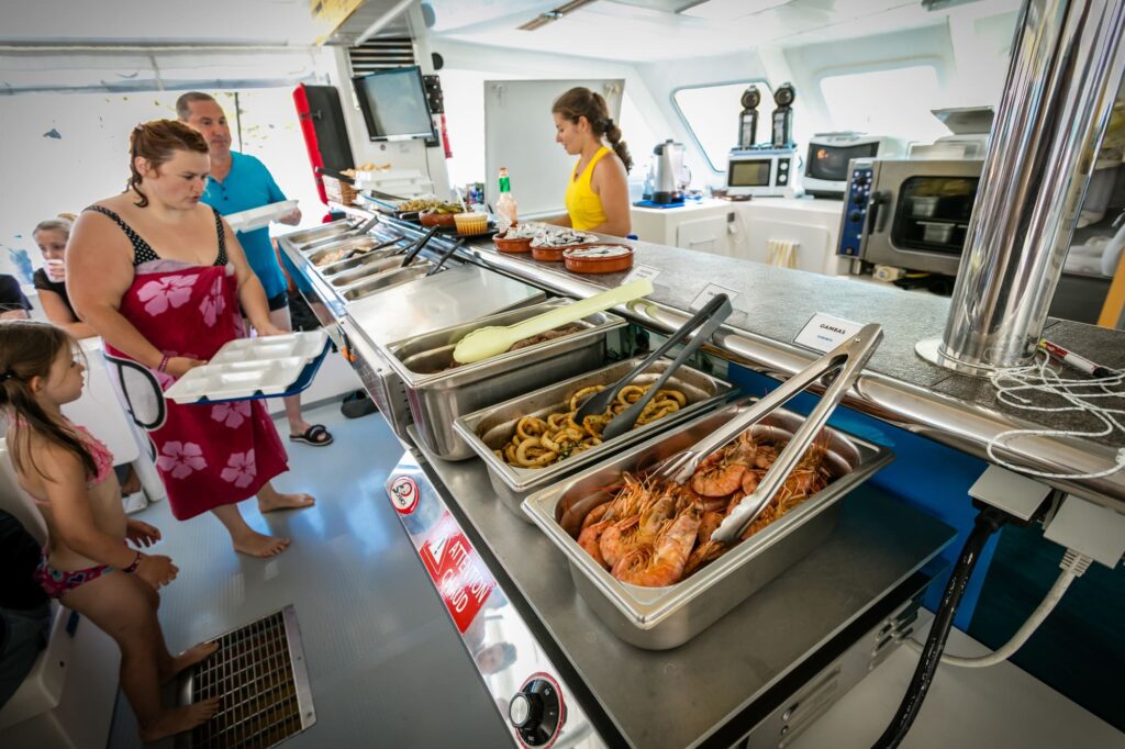 Une famille réunie sur le pont du catamaran se servant des salades fraîches et des grillades préparées à bord lors d'une Sortie bateau Canet