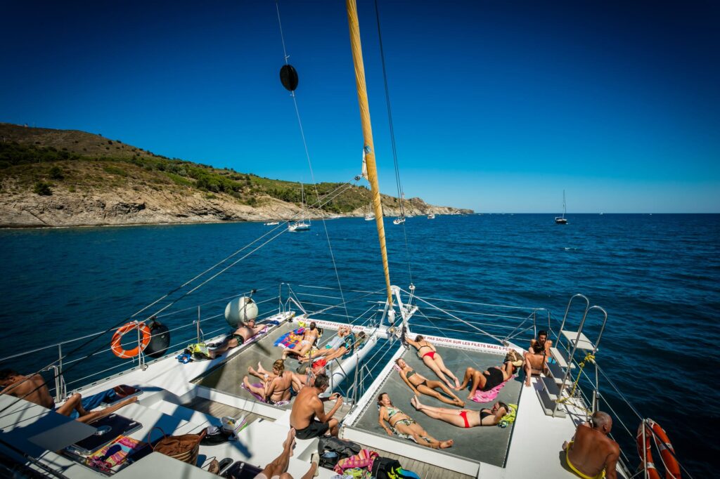 Passagers profitant d'un bain de soleil sur les grands filets à l'avant du catamaran Navivoile, surplombant la mer Méditerranée lors d'une Sortie bateau Canet