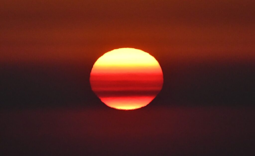 Photo d'une Sortie en Mer au Lever du Soleil au large de La Franqui. Le soleil apparaît comme une boule de feu à travers l'humidité matinale, juste à côté du célèbre Rocher de la Sorcière, lors d'une session d'observation de dauphin à bord du catamaran Navivoile