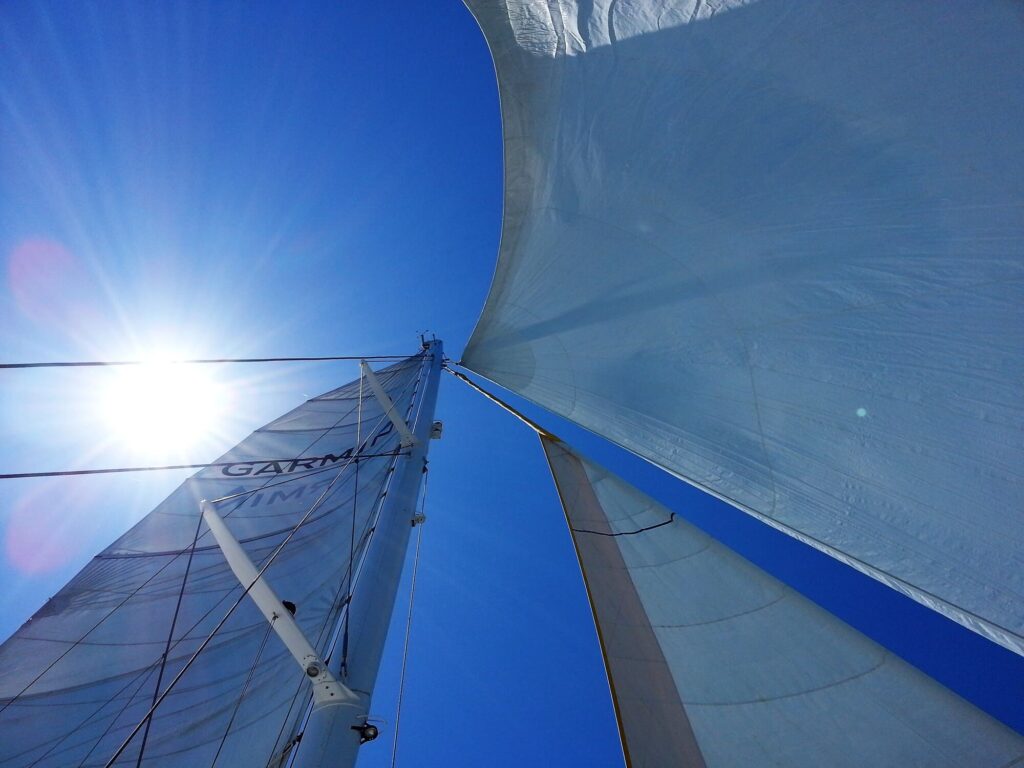 Vue des trois voiles déployées du catamaran Navivoile au niveau de la têtière du mât, avec le soleil traversant la toile au large du Barcarès