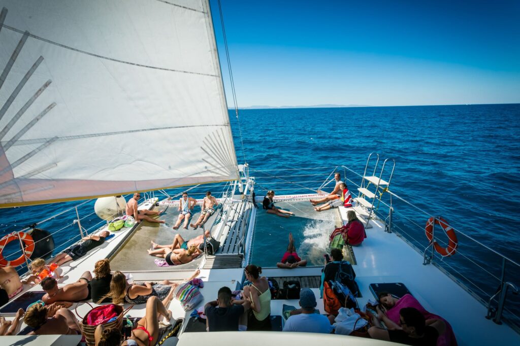 Le catamaran Navivoile naviguant sous voiles par brise de sud-est au large d'Argelès-sur-Mer, avec une vue lointaine sur le massif des Corbières et le Mont Tauch, lors d'une Sortie en mer à Canet-en-Roussillon