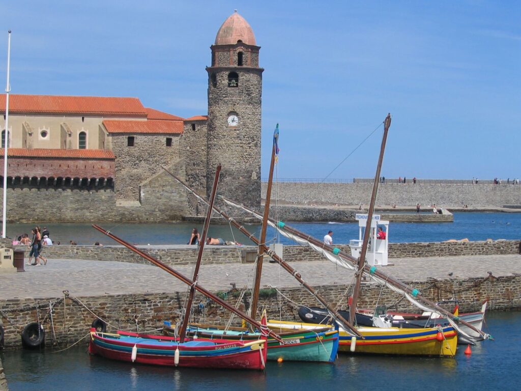 L'église Notre-Dame-des-Anges dominant la plage de Collioure avec des barques de pêcheurs traditionnelles et des baigneurs profitant de la mer