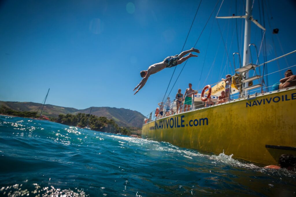 Un passager effectuant un plongeon acrobatique depuis le catamaran Navivoile entre les plages Bernardi et Valenti, lors de l'escale baignade d'une excursion maritime au départ de Canet-en-Roussillon