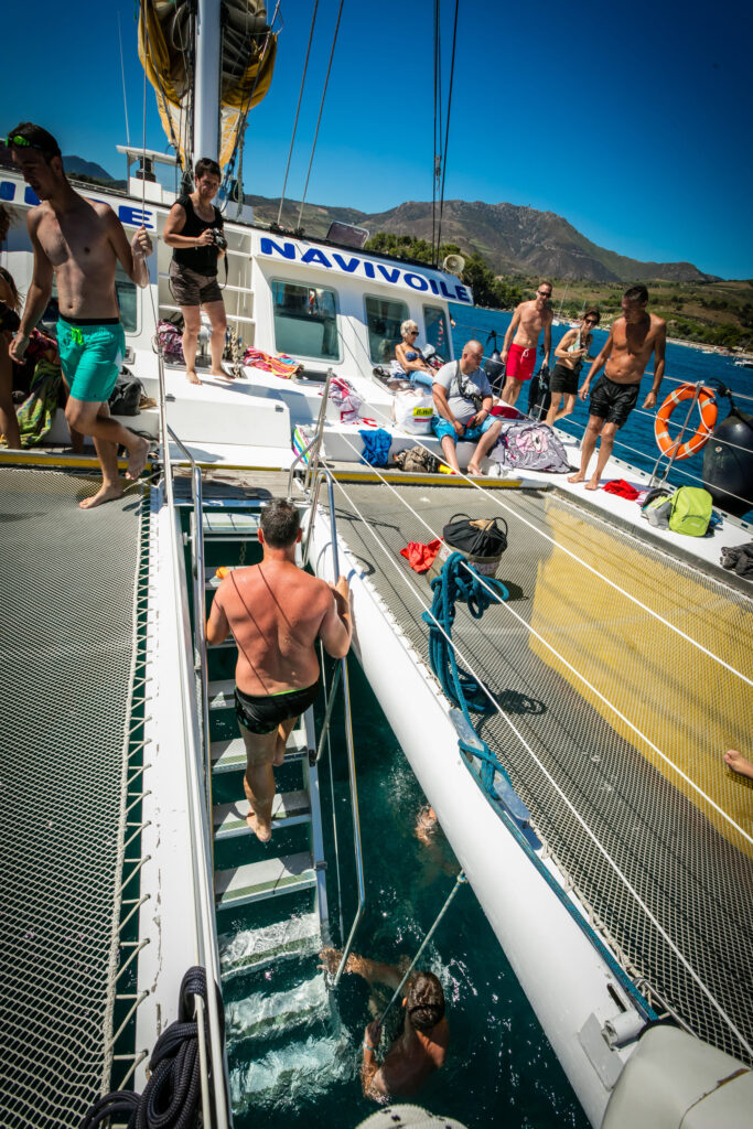 Un nageur remontant à bord via l'escalier central situé entre les deux larges filets de repos du catamaran, lors d'une escale nautique de la croisière dauphins au départ de Canet