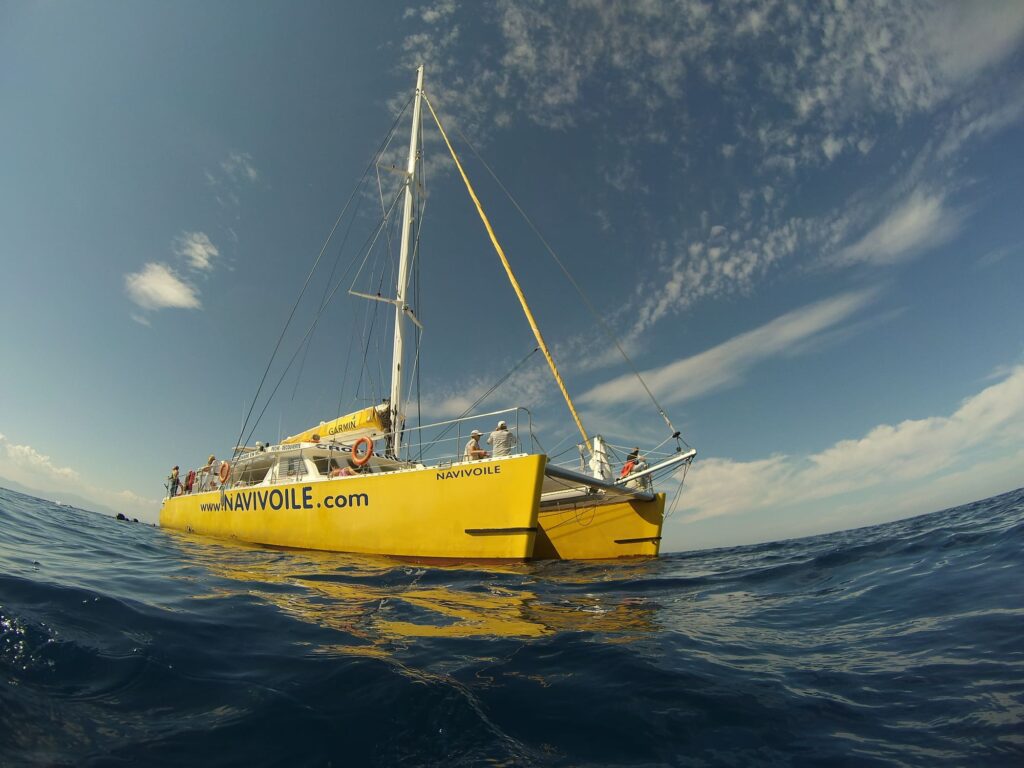 Prise de vue au niveau de l'eau du catamaran Navivoile stationné sur une mer d'huile dans la baie de Paulilles, après le service du déjeuner à bord lors d'une escapade maritime au départ de Canet