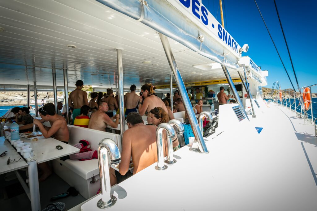 Des passagers déjeunent confortablement à l'ombre dans la nacelle du catamaran Navivoile. Ils profitent d'un buffet libre lors d'une croisière à proximité de la réserve marine de Cerbère-Banyuls-sur-Mer avec le principal catamaran à voile à Canet-en-Roussillon et Port-Vendres