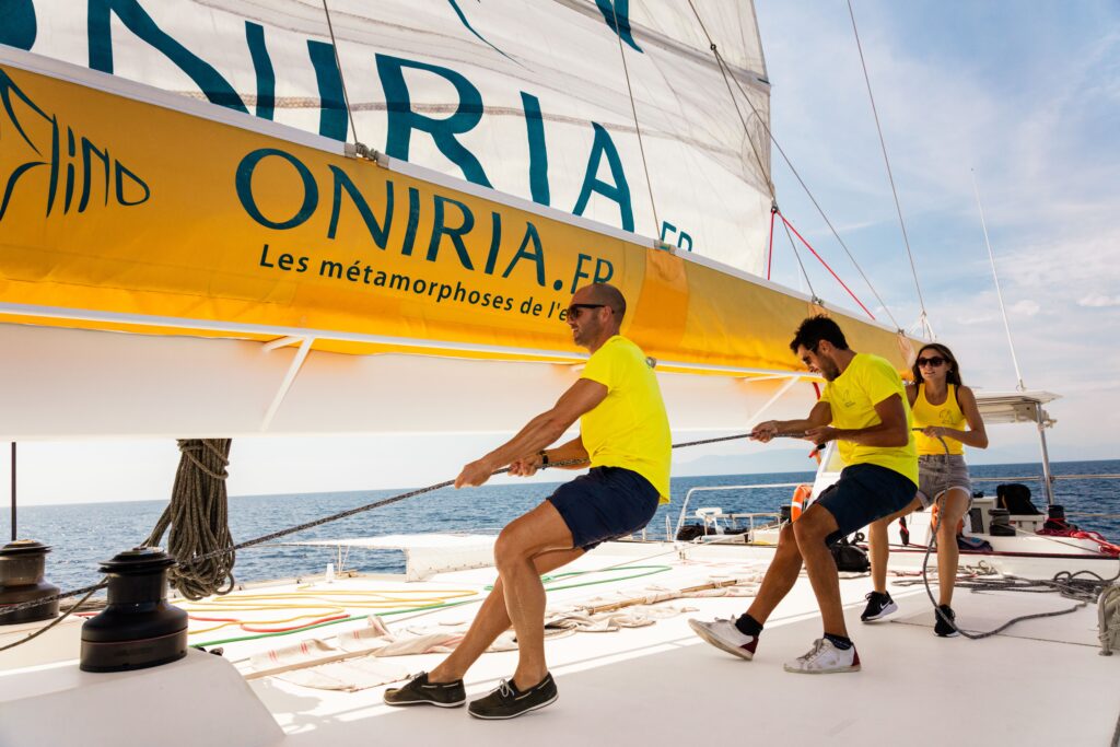 Les marins du catamaran Navivoile en pleine action pour le hissage des voiles sur le roof, devant l'entrée du port de Canet-en-Roussillon. Manœuvre technique sur le principal catamaran à voile à Canet-en-Roussillon et Port-Vendres