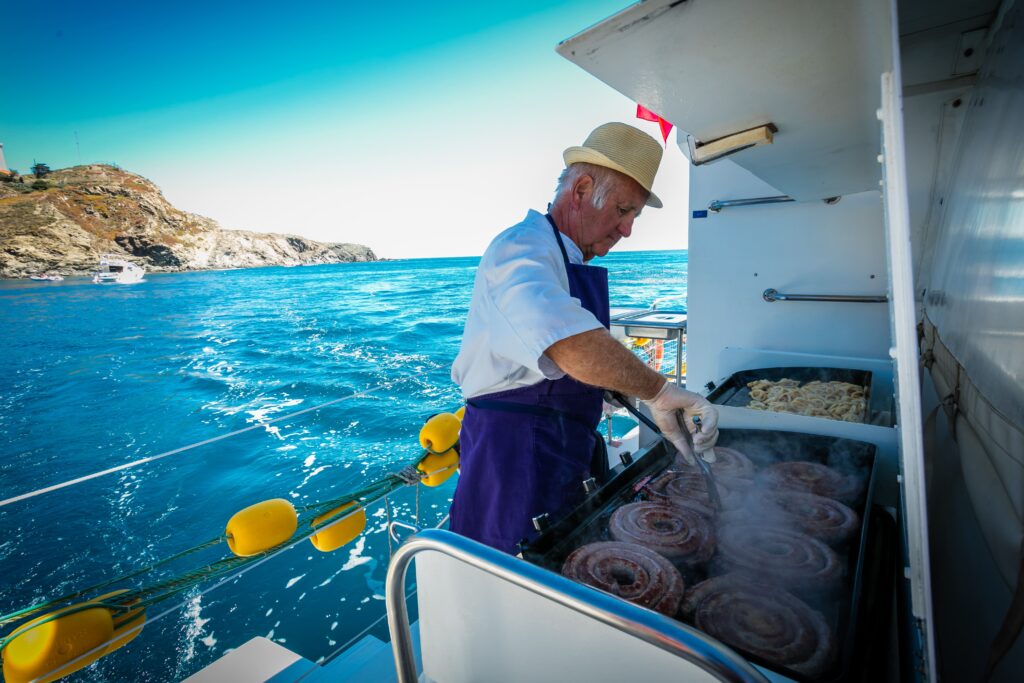Préparation de grillades à la plancha sur le pont du NAVIVOILE lors d'une pause déjeuner pour un séminaire en catamaran privatif le long de la côte rocheuse